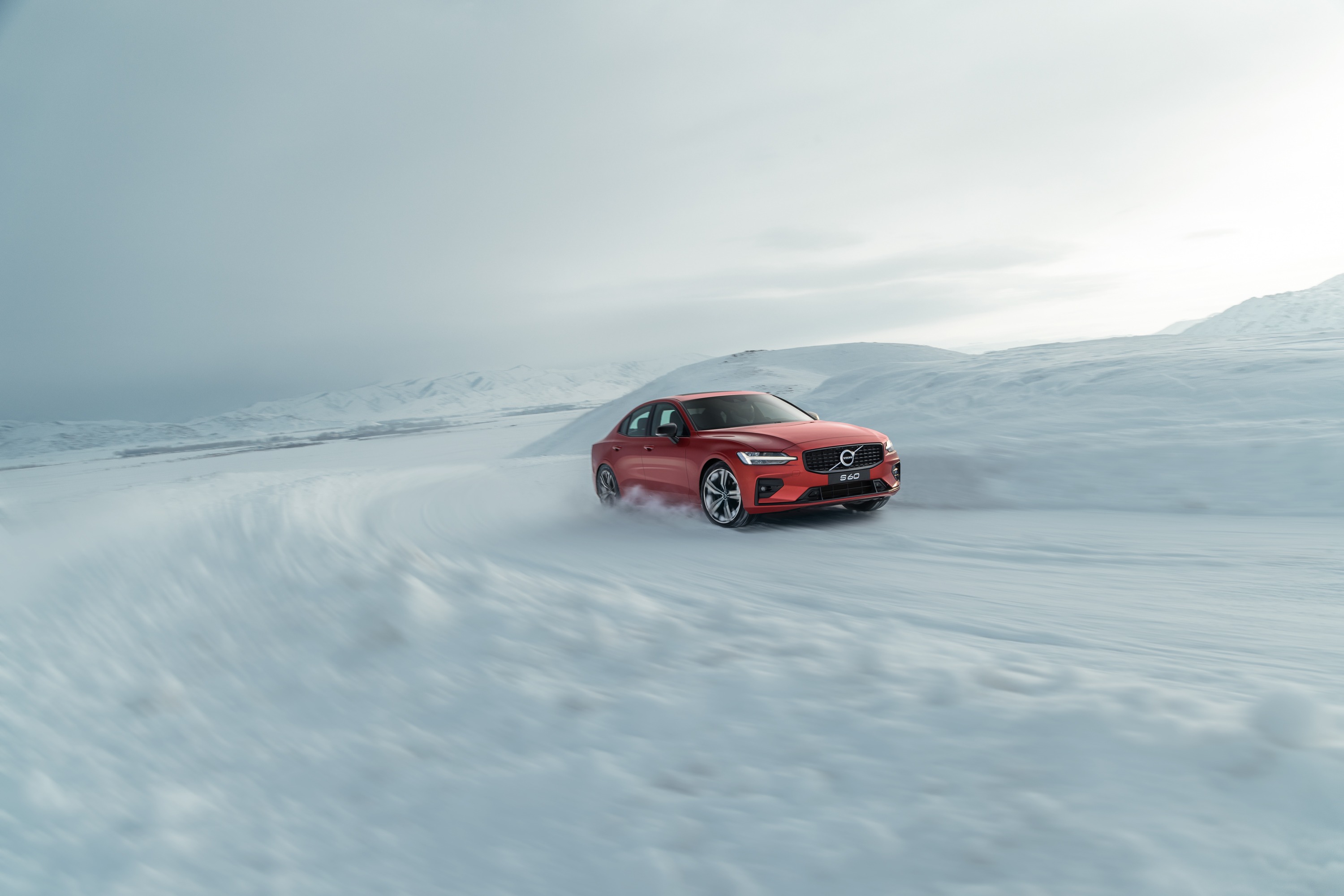 A red car photographed in motion across a snowy mountain road